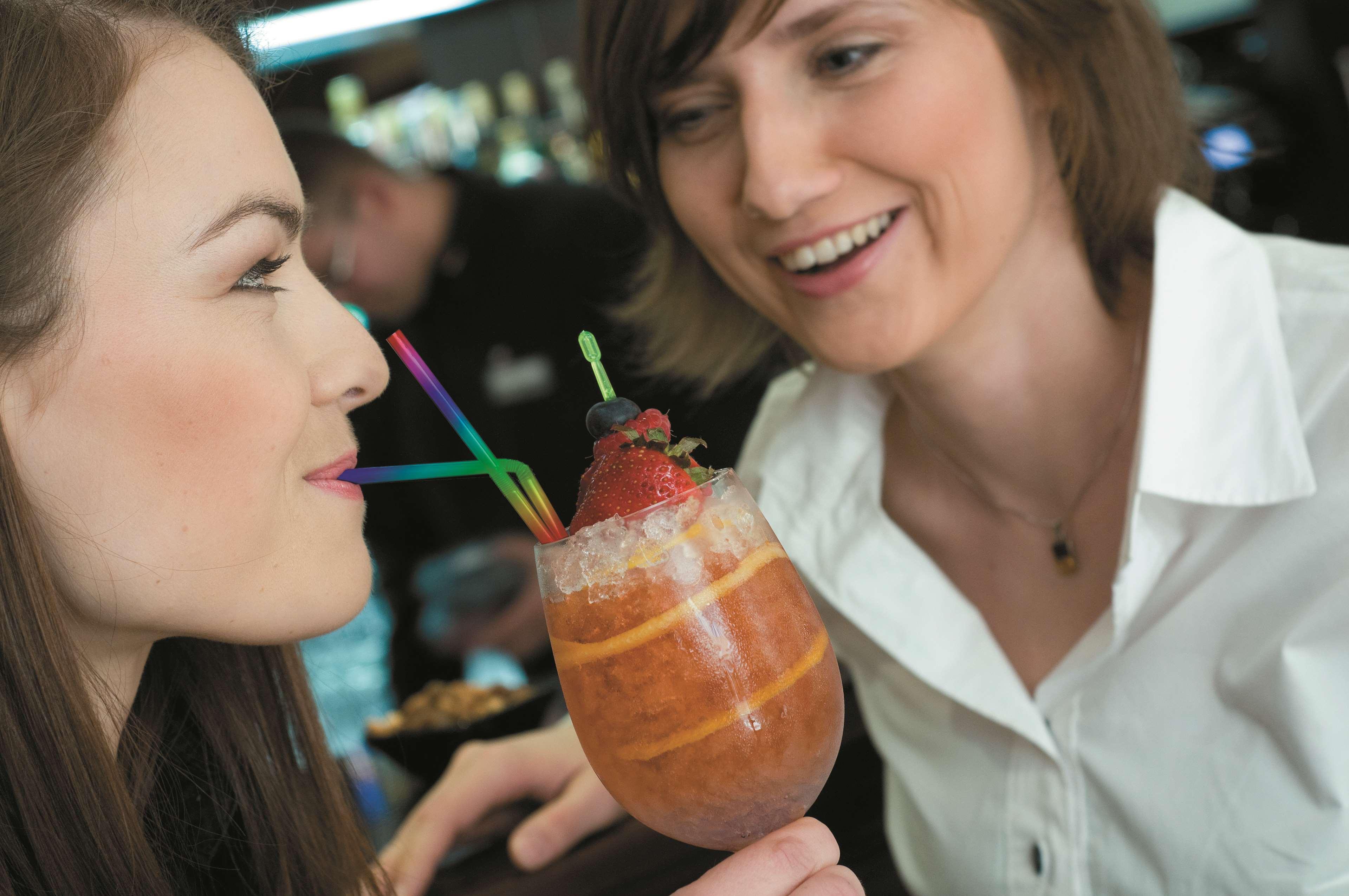 Radisson Blu Hotel, Гданск Екстериор снимка The photo shows two women engaging with each other, smiling and enjoying a moment together. One woman is holding a colorful drink in a large glass adorned with ice, fruit, and multiple straws. The other woman looks on with a friendly expression, cont