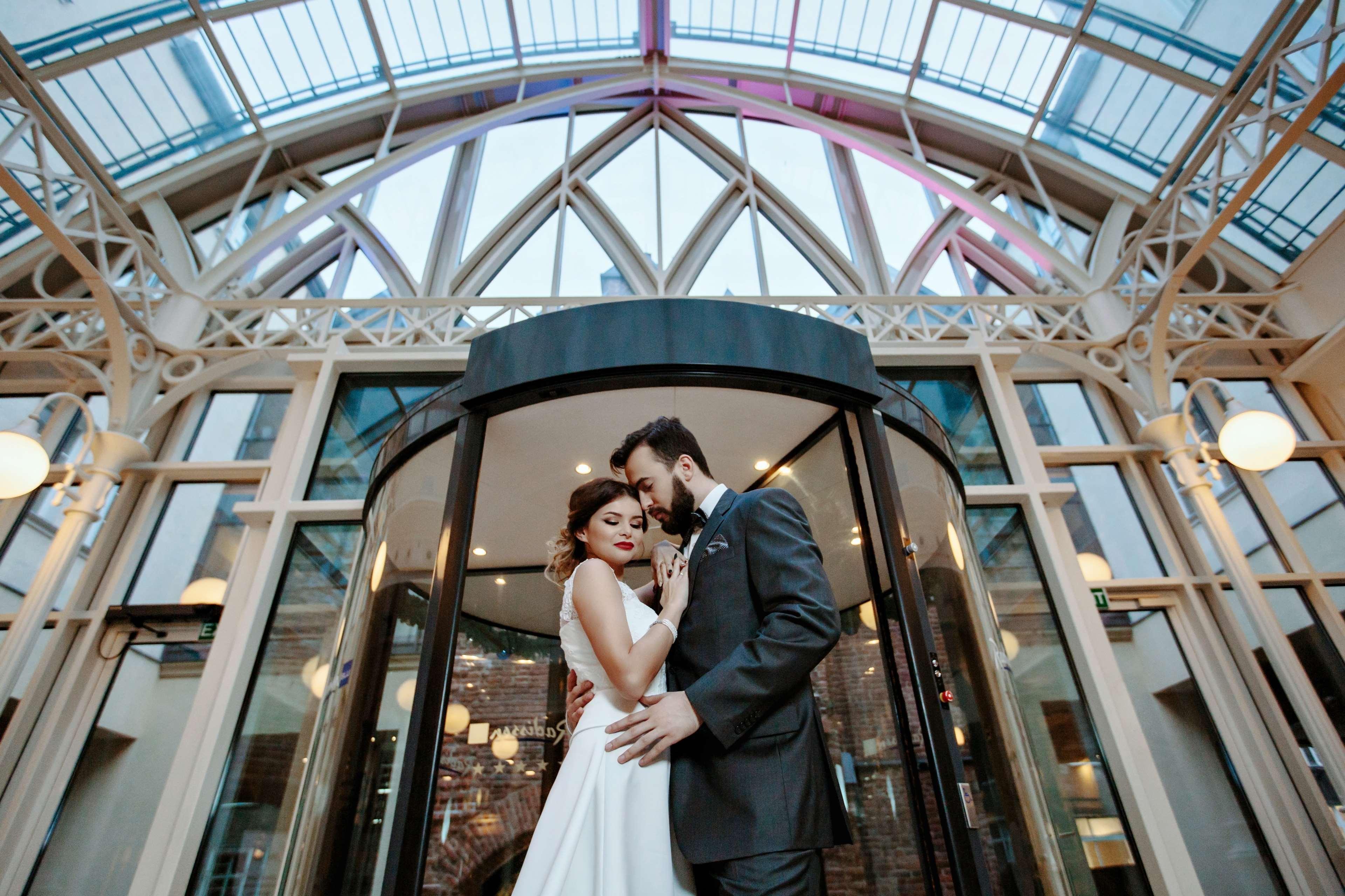 Radisson Blu Hotel, Гданск Екстериор снимка The photo shows a romantic scene featuring a couple in formal attire, likely celebrating their wedding. They are positioned in front of a round glass door, which is partially open. The couple is standing close together, with their foreheads touching,