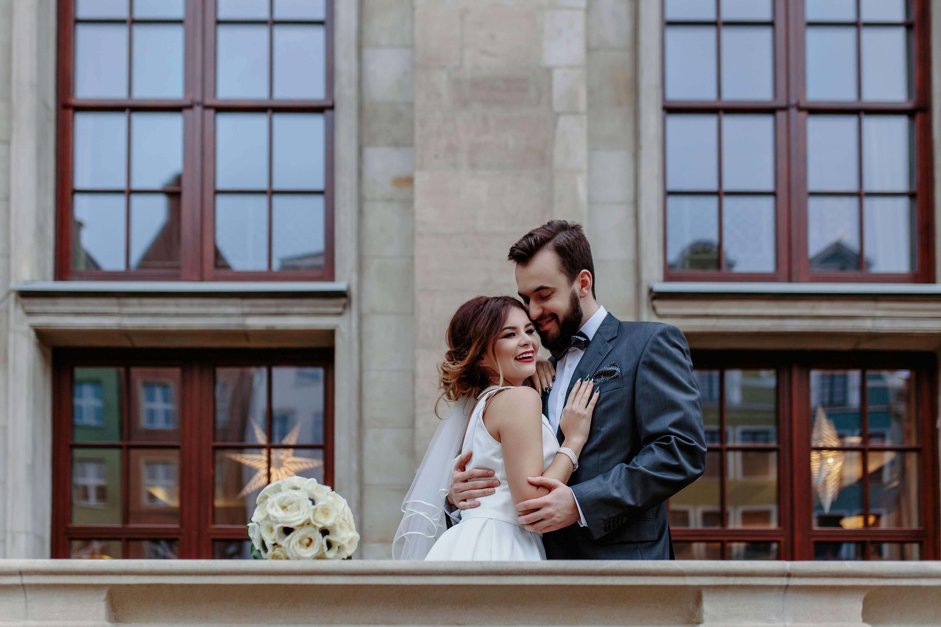 Radisson Blu Hotel, Гданск Екстериор снимка The photo depicts a joyful couple embracing in a romantic pose. The woman, dressed in a white wedding gown, is smiling and appears to be looking at the man, who is wearing a dark suit. They are standing in front of large windows, which suggest an ele