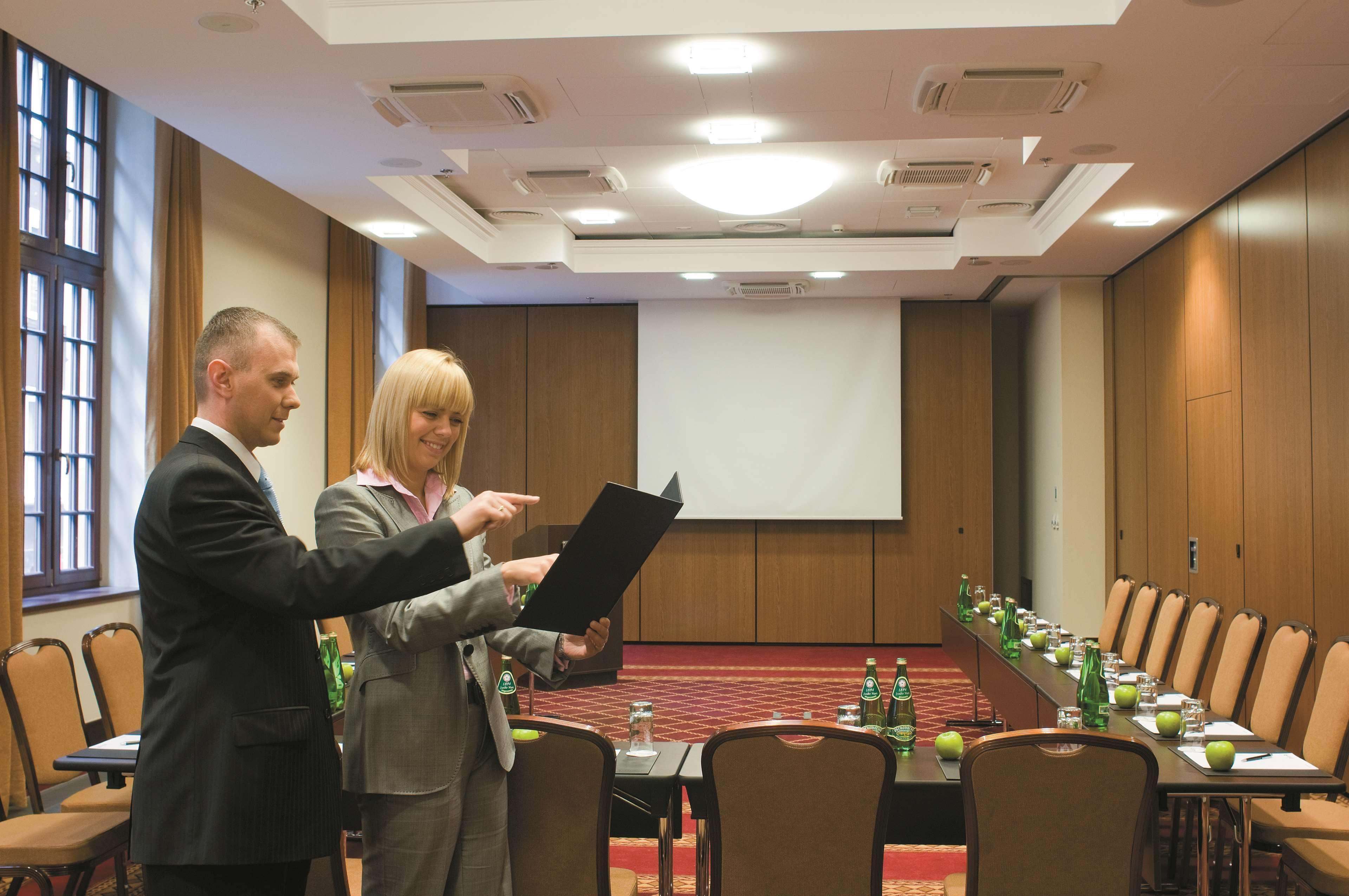 Radisson Blu Hotel, Гданск Съоръжения снимка The image shows a professional meeting room set up for a conference or presentation. There are two people in formal attire engaged in discussion; one is holding a document or folder while the other is pointing at it. The room features a large screen 