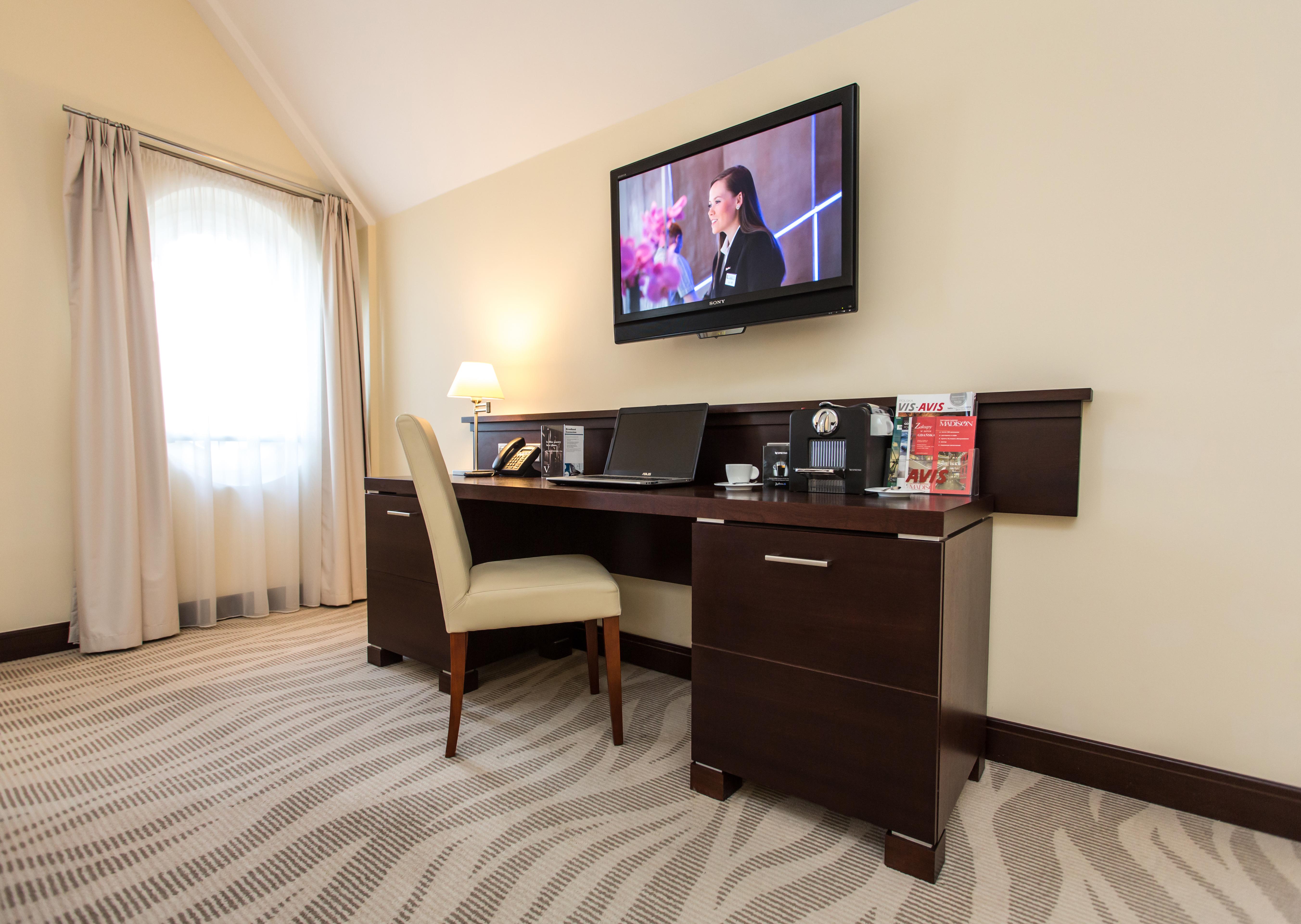 Radisson Blu Hotel, Гданск Екстериор снимка The photo depicts a corner of a room featuring a stylish desk with a chair and a television mounted on the wall above. The desk has various items on it, possibly including a telephone, clock, and some decorative elements or stationery. There is a lam