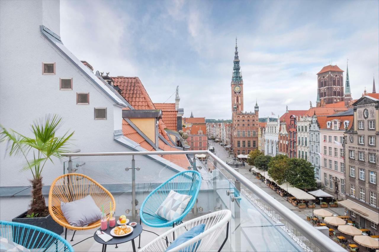 Radisson Blu Hotel, Гданск Екстериор снимка The photo shows a stylish balcony overlooking a scenic urban landscape. There are two colorful chairs in blue and white, positioned around a small table. On the table, there are desserts and drinks, suggesting a cozy spot for relaxation. In the backg