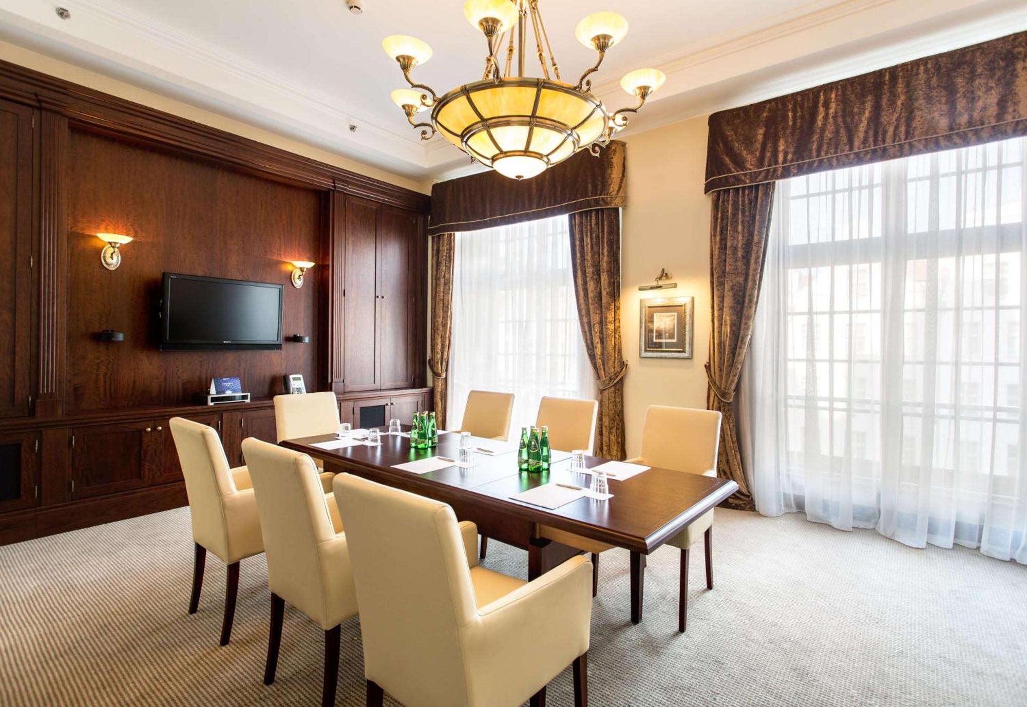 Radisson Blu Hotel, Гданск Екстериор снимка The photo shows a well-furnished conference room. It features a large wooden table surrounded by six cream-colored chairs. On the table, there are several green glass bottles of water. The room is well-lit with a decorative chandelier hanging from th