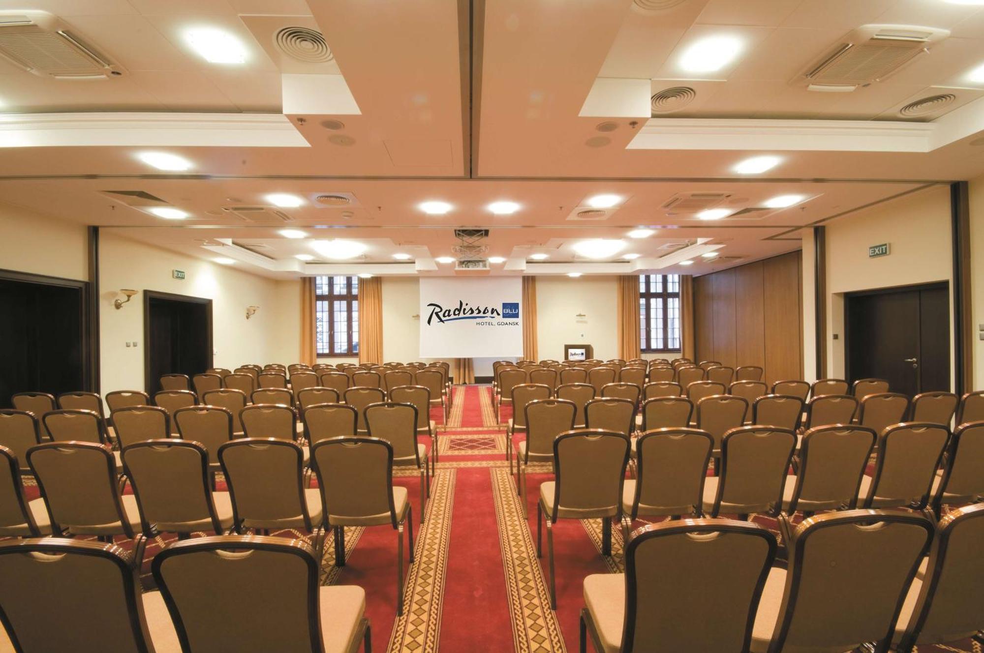 Radisson Blu Hotel, Гданск Екстериор снимка The photo shows the interior of a conference room or event space. It features rows of brown chairs arranged neatly, facing towards the front where a stage or presentation area is set up. There is a carpet running down the center of the room, and the 