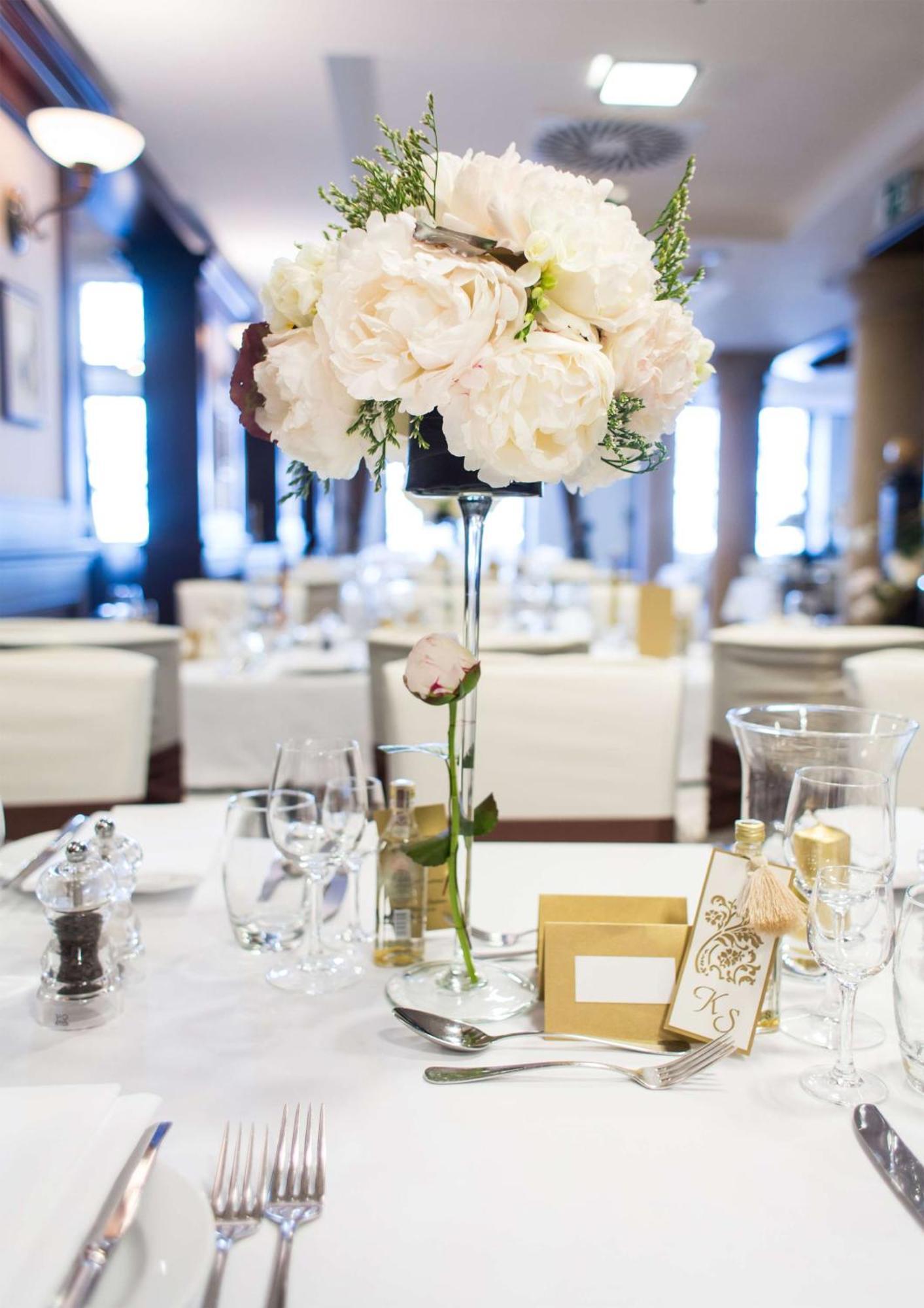Radisson Blu Hotel, Гданск Екстериор снимка The photo depicts a beautifully arranged table setting, likely for a formal event or celebration. At the center of the table is a tall floral arrangement featuring soft pink peonies and greenery, elegantly placed in a clear vase. Surrounding the cent