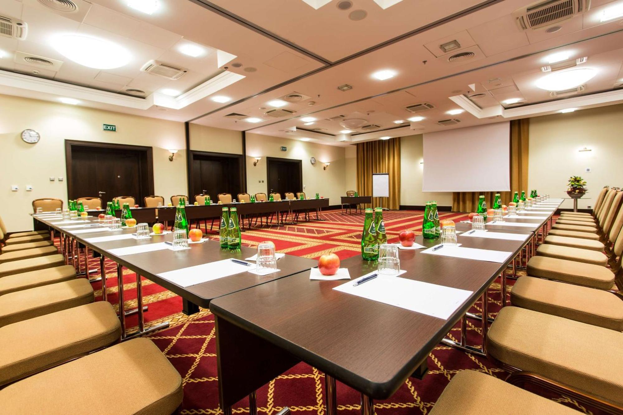 Radisson Blu Hotel, Гданск Екстериор снимка The photo shows a conference room set up for a meeting or seminar. Long tables are arranged in a U-shape, surrounded by beige chairs. Each table has green glass bottles of water, small glasses, and apples placed on it. There are also sheets of paper 