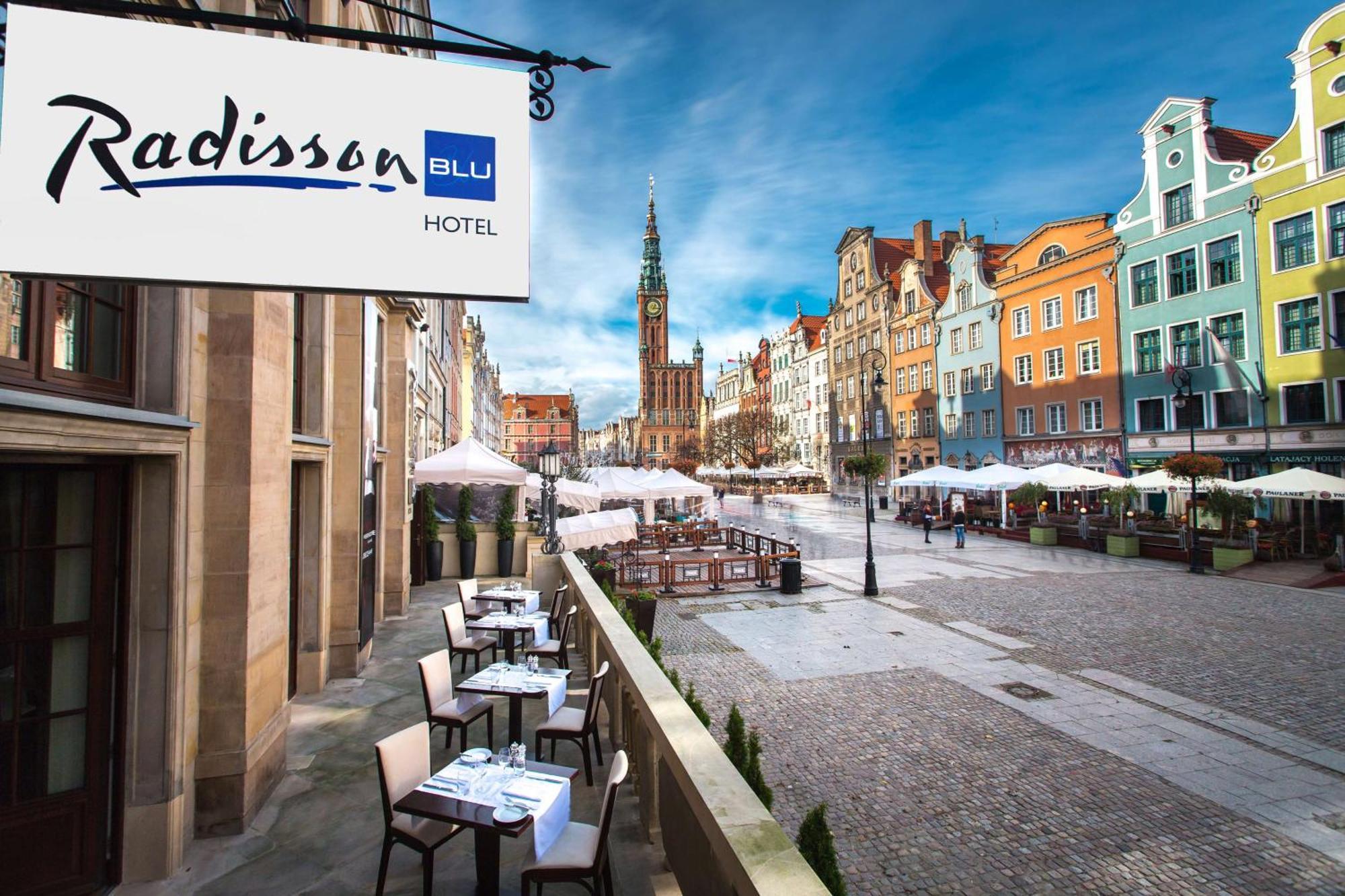 Radisson Blu Hotel, Гданск Екстериор снимка The photo shows a view of the Radisson Blu Hotel, which is situated in a vibrant, picturesque area. The image features an outdoor seating arrangement with tables and chairs, likely part of a restaurant or café. In the background, colorful historic bu