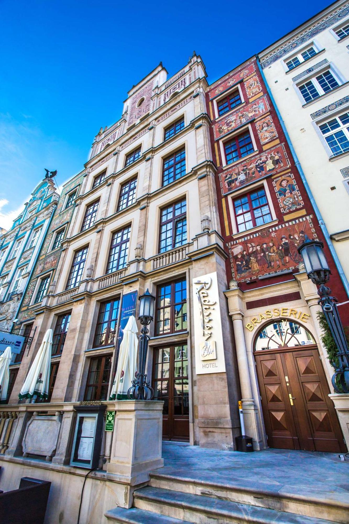 Radisson Blu Hotel, Гданск Екстериор снимка The photo shows a historic building with a richly decorated facade. The architecture features large windows and intricate details, including murals or painted scenes on the walls. There is a sign that indicates a brasserie, suggesting that this locat